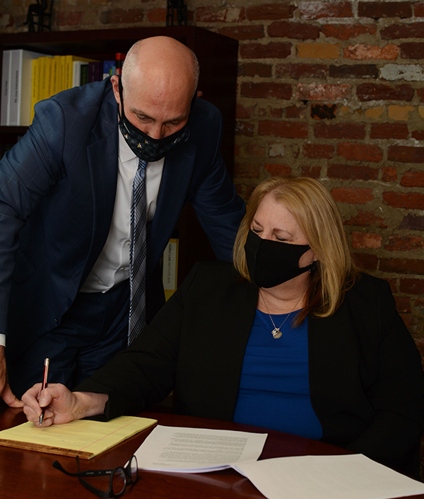 Michael Zunder assists Tracy Schaffner with writing, both wearing black face masks for protection.